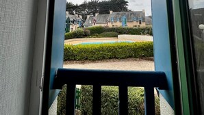 A view from a balcony with a railing, overlooking a courtyard with neatly trimmed hedges and a small pool.