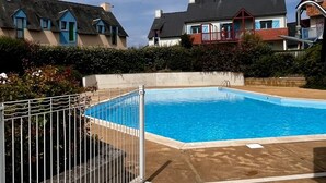 A swimming pool with a metal fence, surrounded by houses with distinct architectural styles.