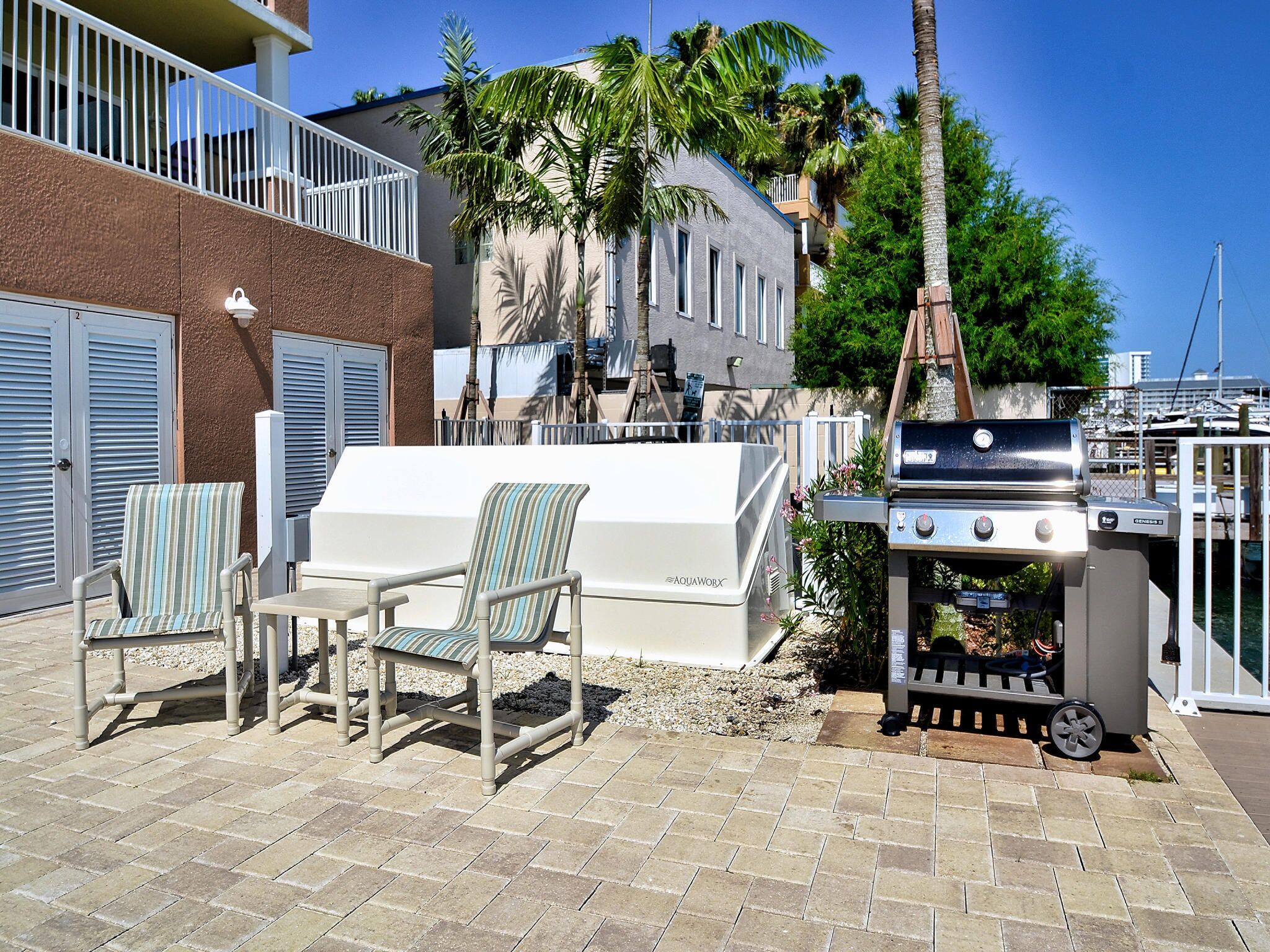 An outdoor patio with a grill, two striped chairs, and a table.