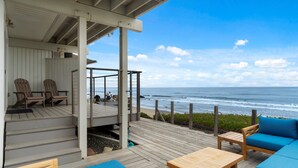 Terraza de madera con mobiliario exterior, una escalera que lleva a un espacio cubierto y vistas al océano.