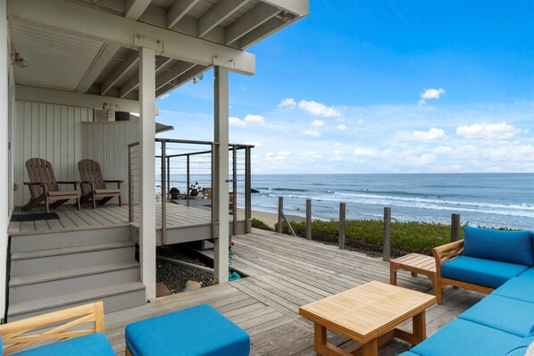 A wooden deck with outdoor seating, a staircase leading to a covered area, and a view of the ocean.
