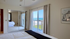 Ein Hotelzimmer mit Bett, einem großen Fenster mit Blick auf den Strand und einer Schiebetür, die auf einen Balkon führt.