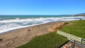 Una playa con olas, un área con césped y un banco.