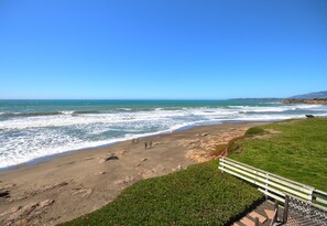 Una playa con olas, un área con césped y un banco.
