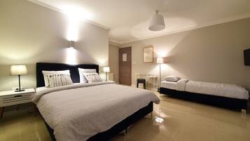 Une chambre d’hôtel moderne avec un grand lit, un lit plus petit, des tables de chevet avec des lampes, un bureau et une chaise.