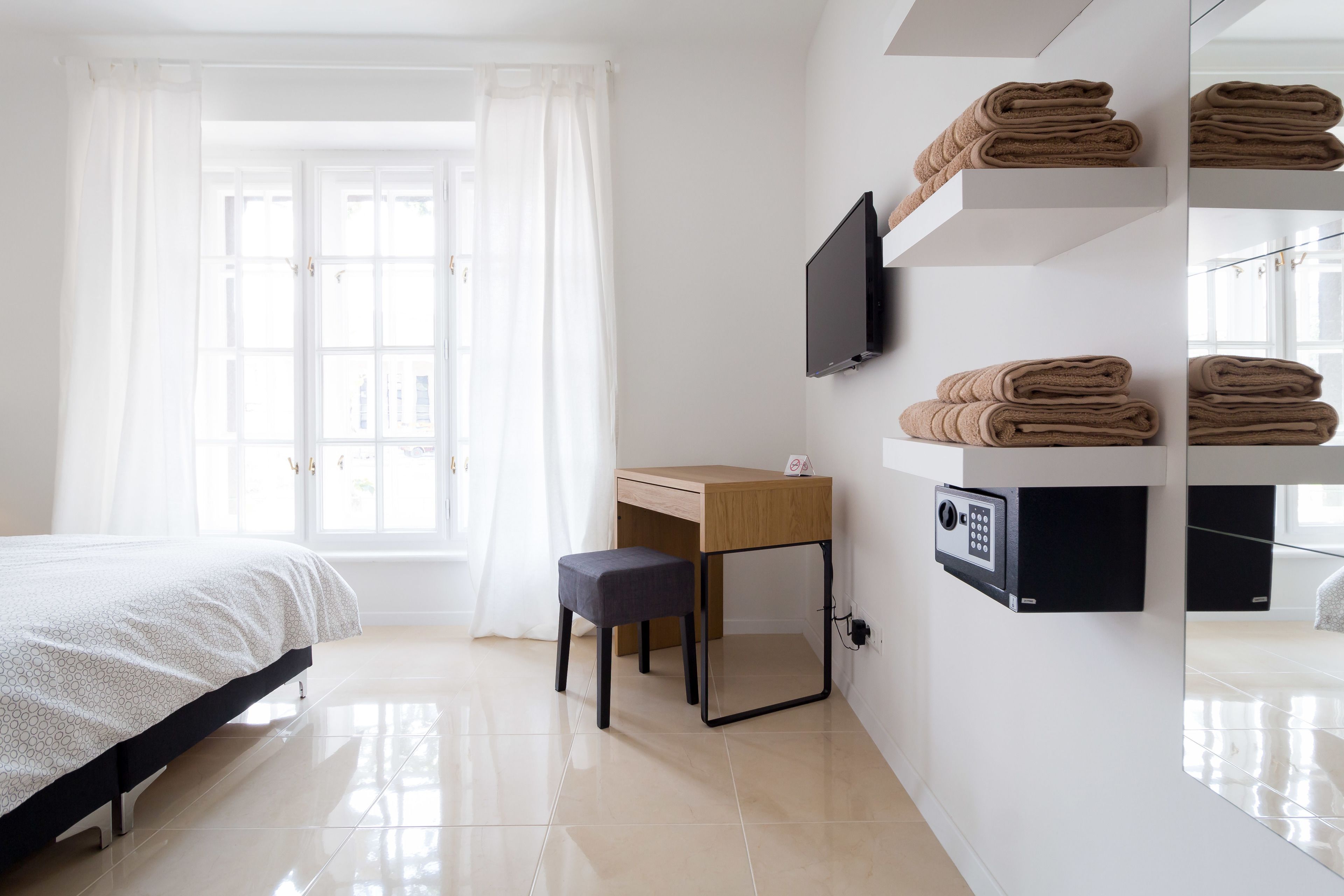 Ein Hotelzimmer mit Bett, Schreibtisch, Stuhl, Fernseher und einem fest installierten Safe.