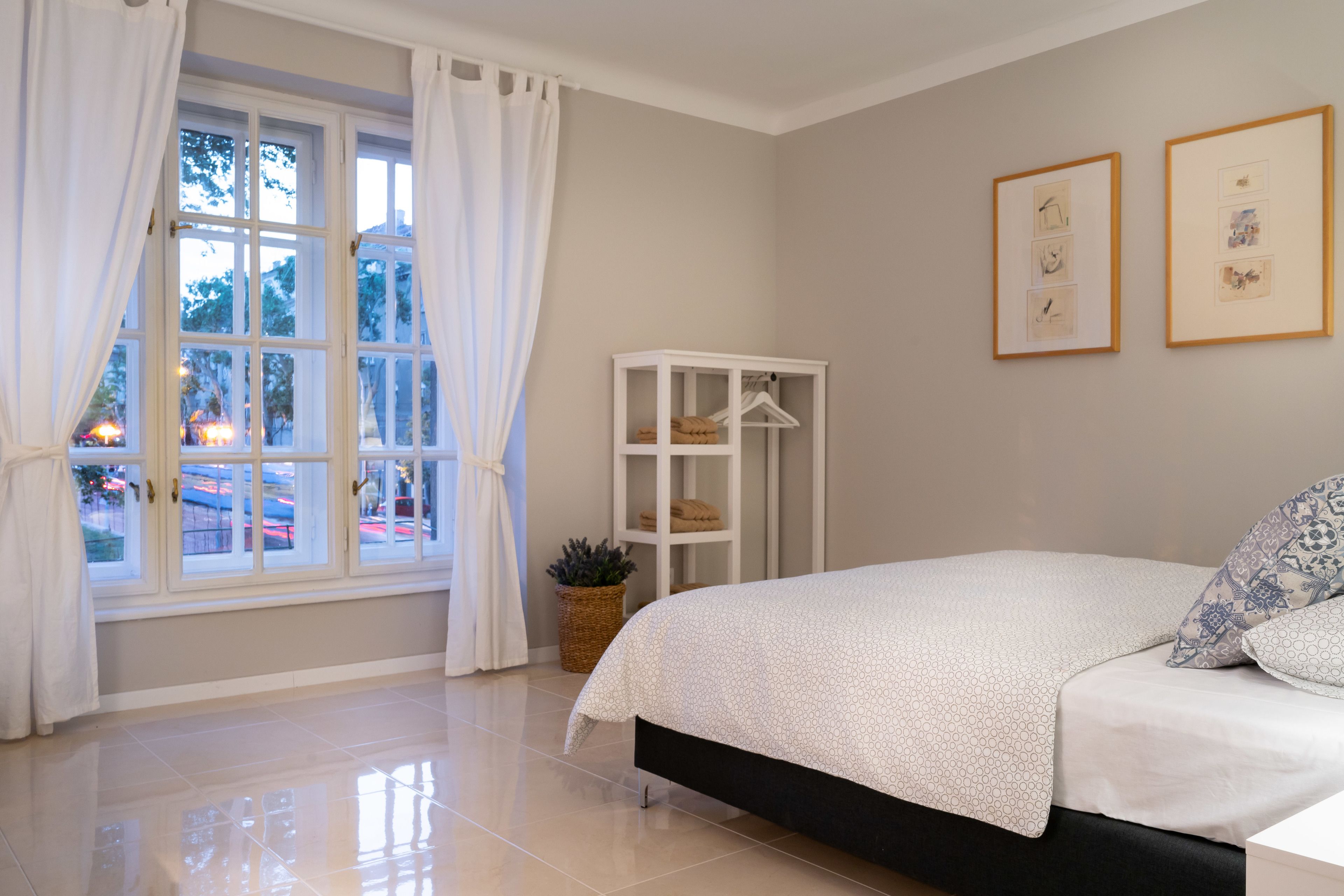Un dormitorio con cama, ventana con cortinas, un armario blanco y dos cuadros en la pared.