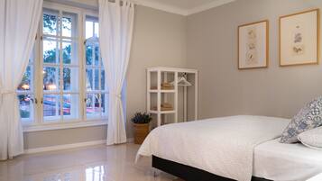 Un dormitorio con cama, ventana con cortinas, un armario blanco y dos cuadros en la pared.