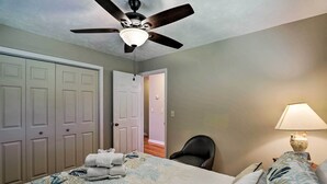 A bedroom with a bed, a ceiling fan, a chair, a lamp, and a door leading to another room. - Spacious Mount Pleasant Home: 5 Mi to Beach (Mount Pleasant)