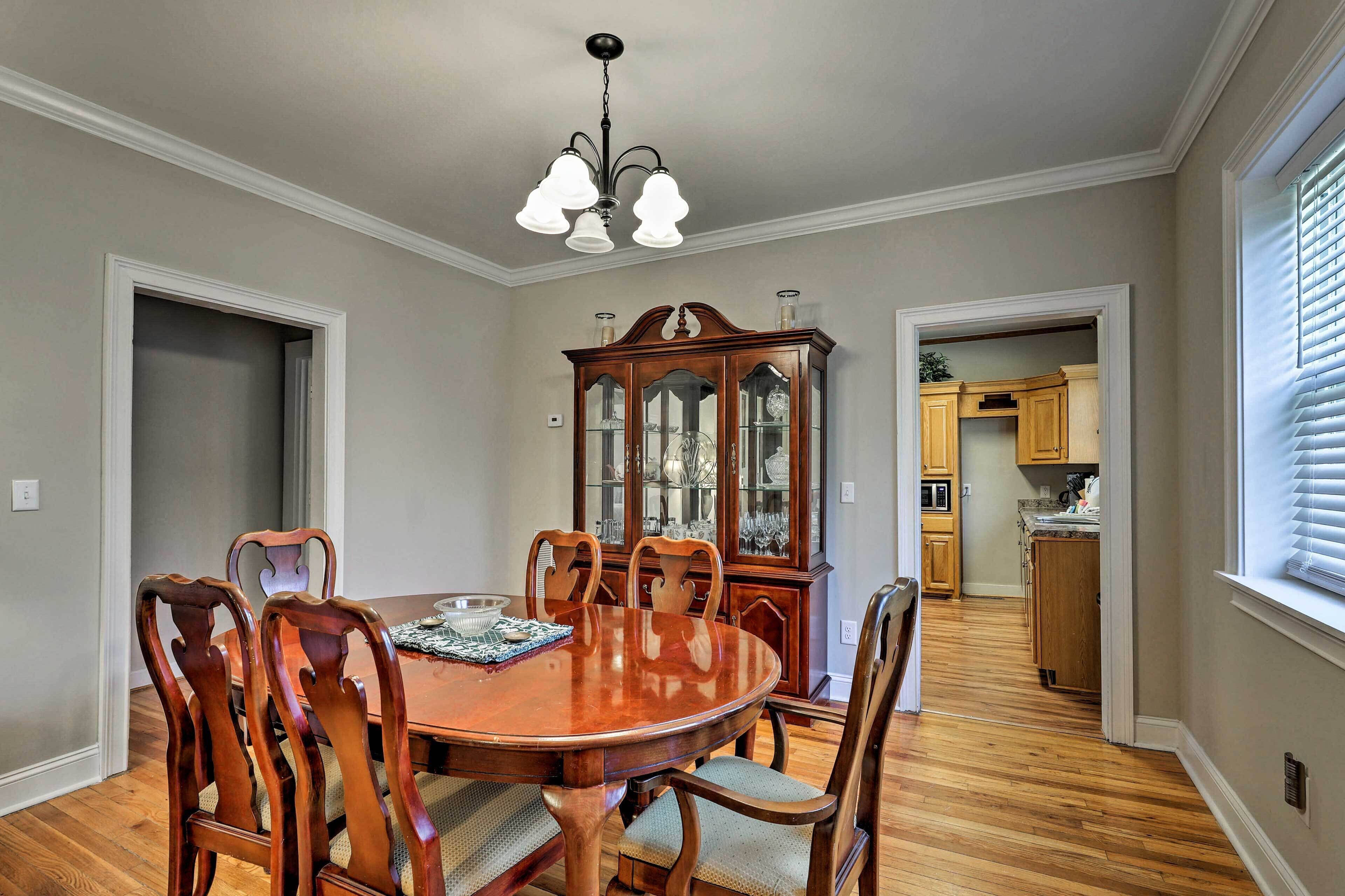 A dining room with a wooden table and chairs, a china cabinet, and a kitchen in the background.