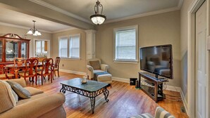 A spacious living room with hardwood floors, a dining area with wooden furniture, a television, and a chandelier. - Spacious Mount Pleasant Home: 5 Mi to Beach (Mount Pleasant)