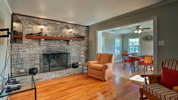 A living room with a brick fireplace, wooden flooring, a glass coffee table, and a red sofa. - Spacious Mount Pleasant Home: 5 Mi to Beach (Mount Pleasant)