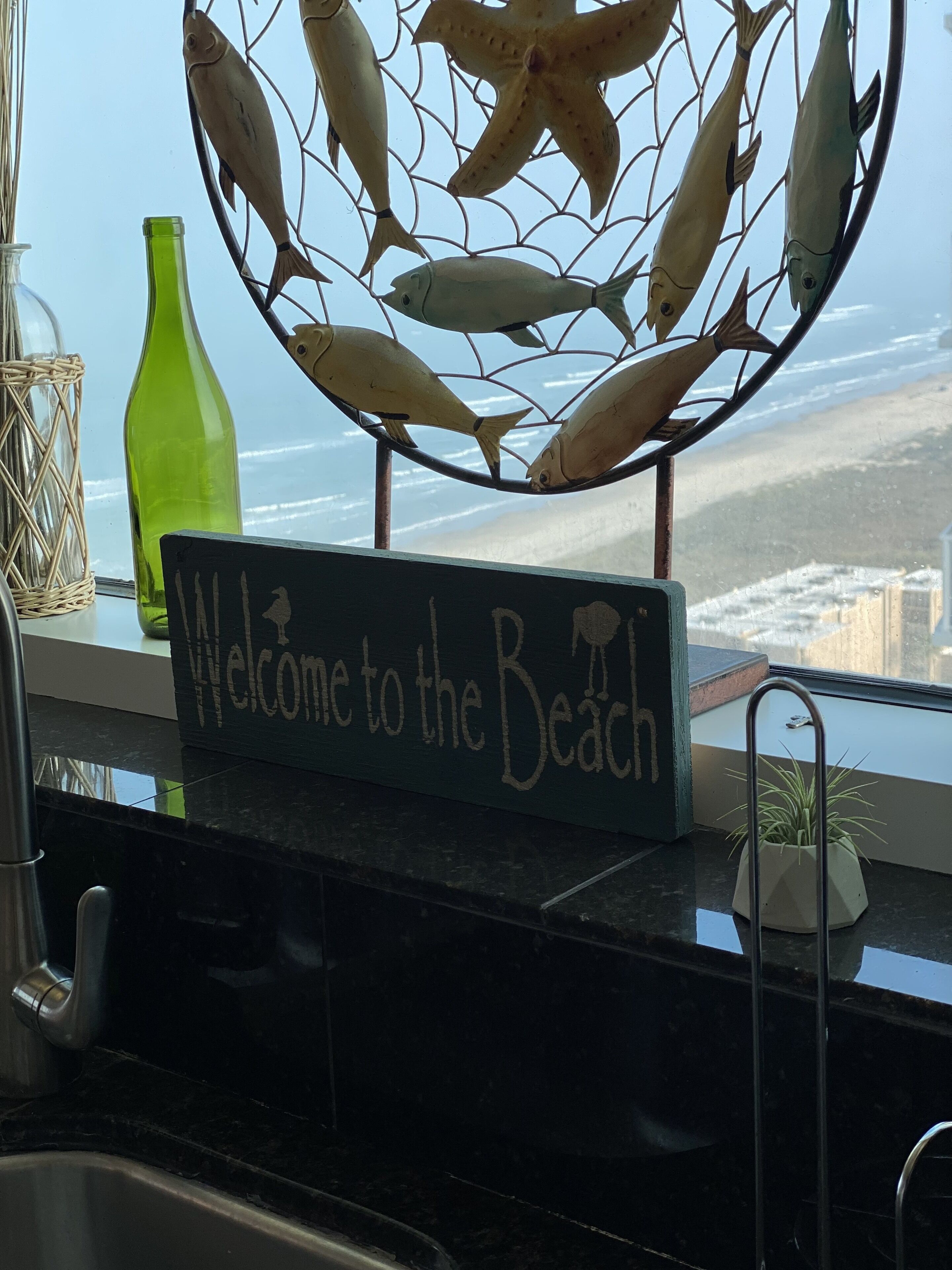 A kitchen counter with a sign reading "Welcome to the Beach," a green bottle, and a decorative fish wireframe.