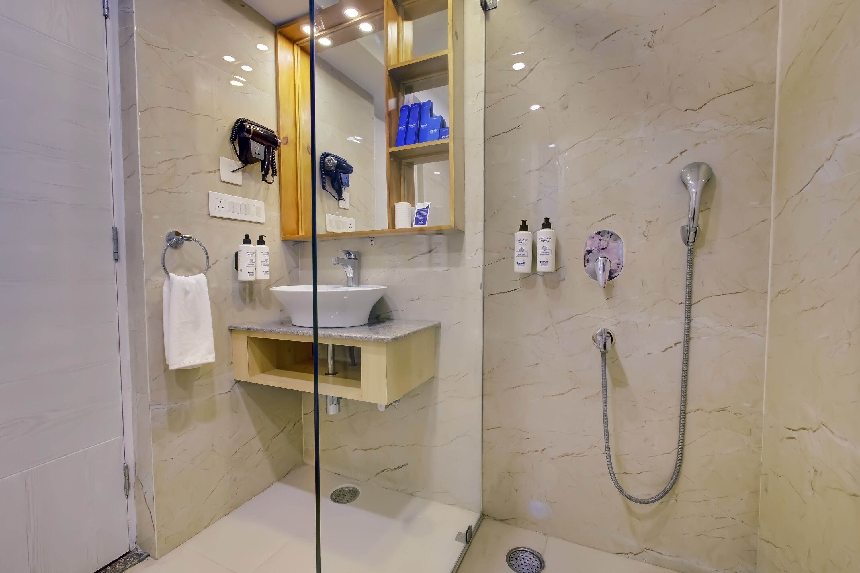 A modern bathroom with a marble floor, a sink with a vanity, a glass shower enclosure, and a mirror with a hairdryer and blue boxes on the wall.