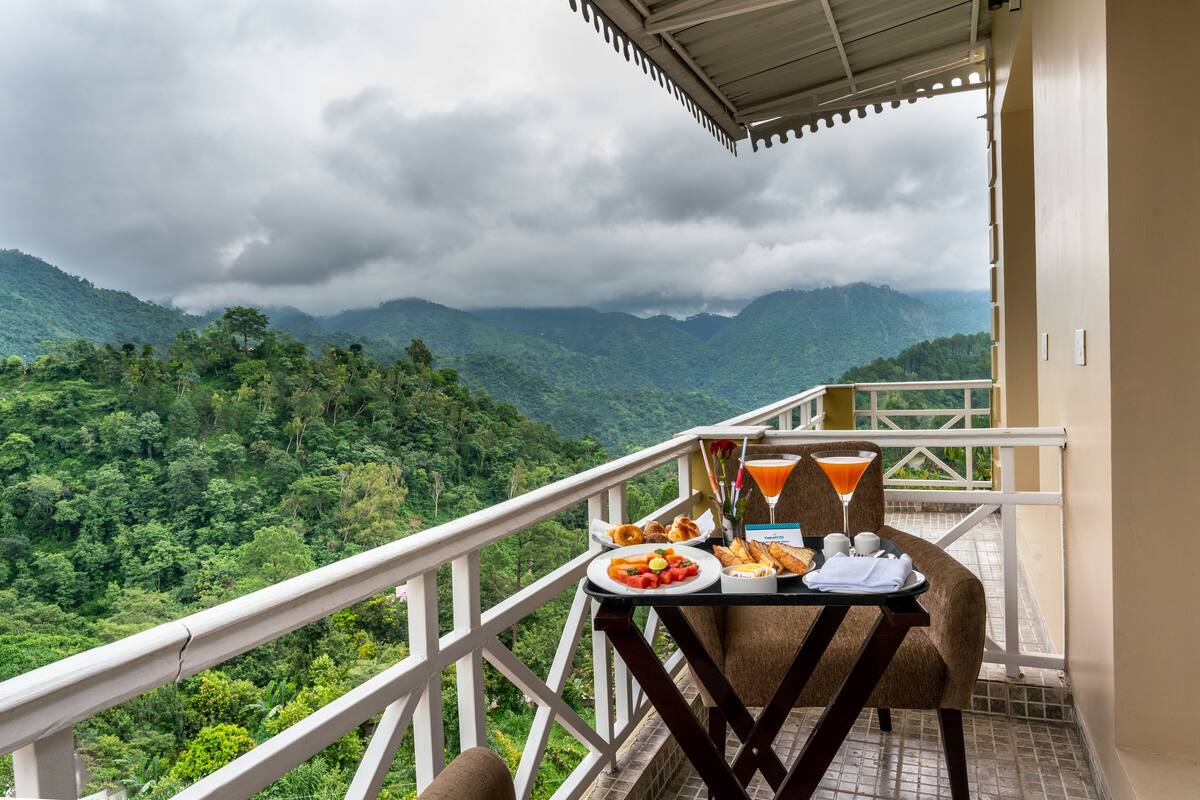 A balcony with a table set for breakfast, overlooking a lush green valley and mountains.
