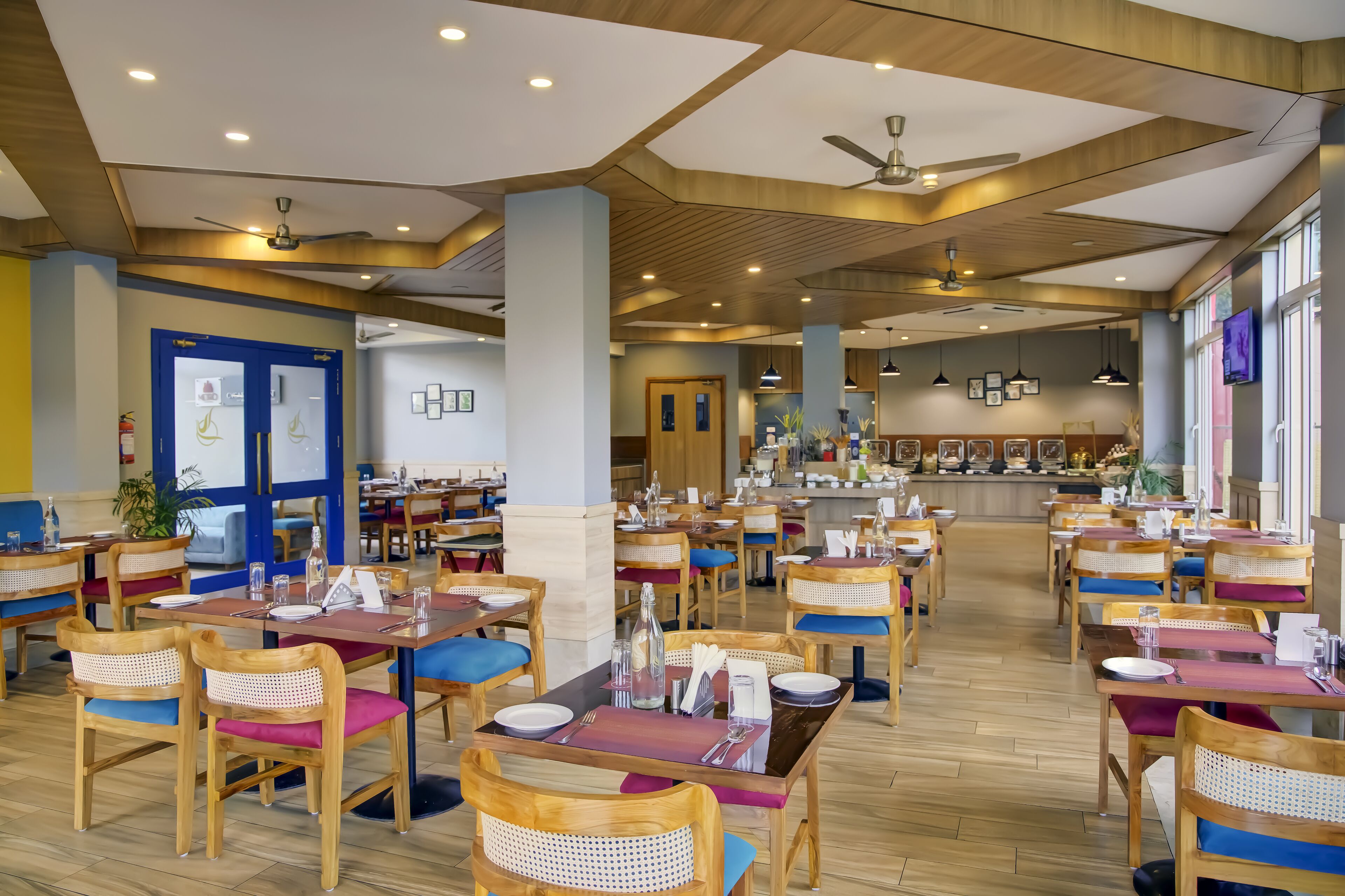 A spacious restaurant with wooden tables and chairs, a bar area, and large windows.