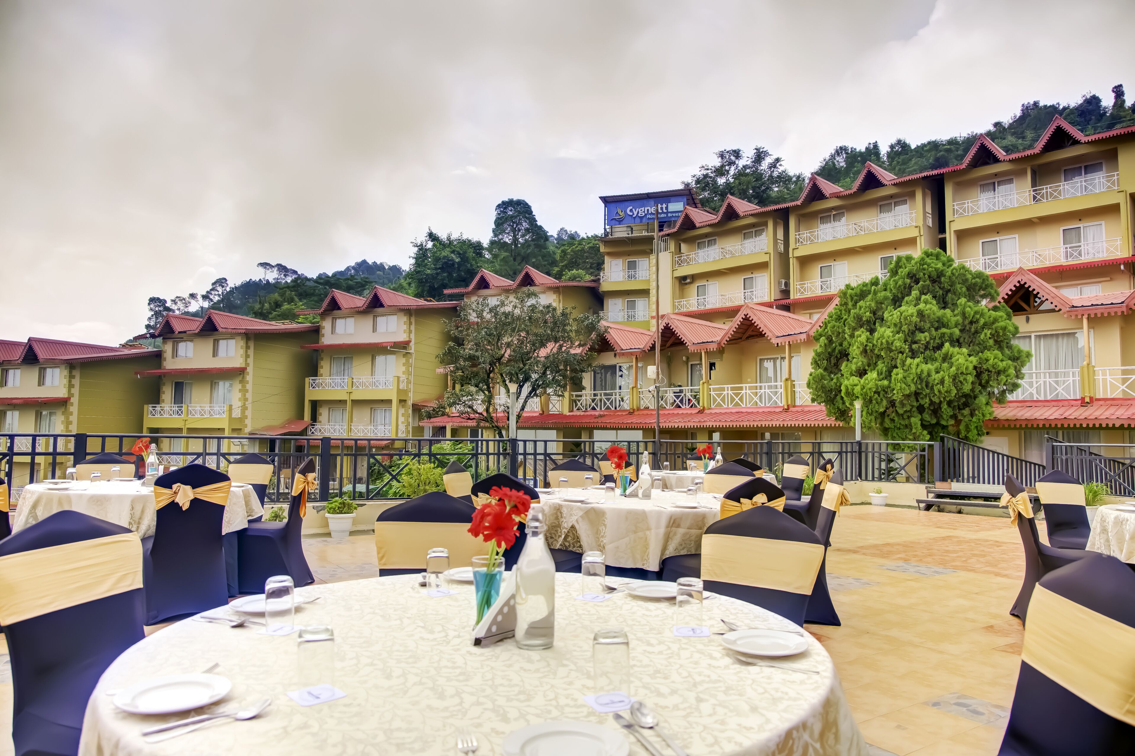 A hotel with outdoor dining areas, multiple balconies, and a mountainous backdrop.