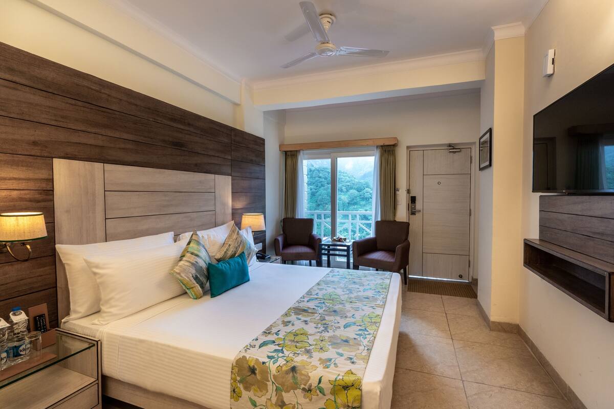A hotel room with a large bed, a ceiling fan, a TV, a desk with a lamp, and a view of the outdoors.