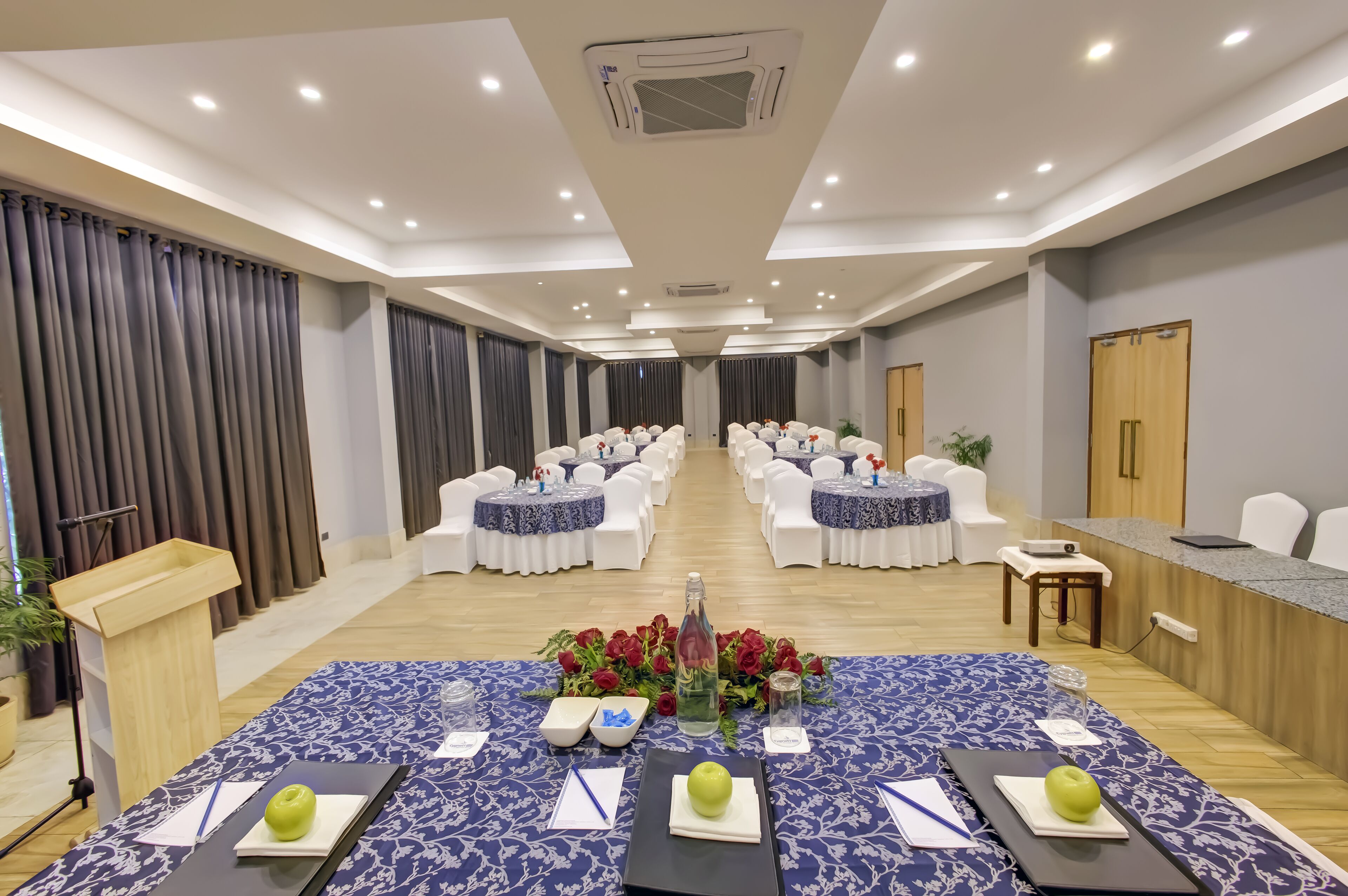 A conference room with round tables, white chairs, a podium, and a reception desk.