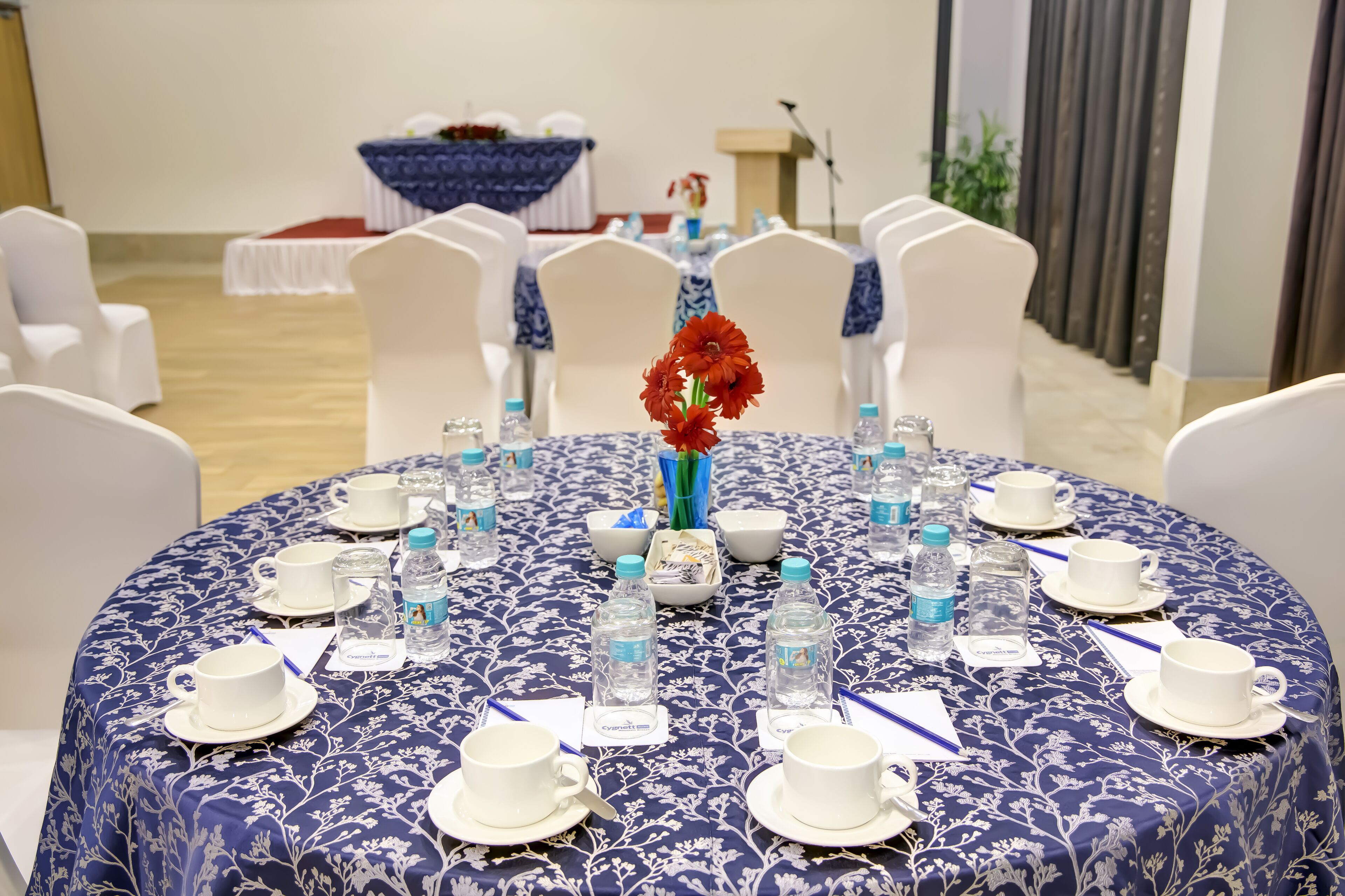 Una mesa redonda con mantel floral, sillas blancas y botellas de agua.
