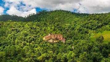 A hotel with multiple floors and balconies, surrounded by dense forest and hills.