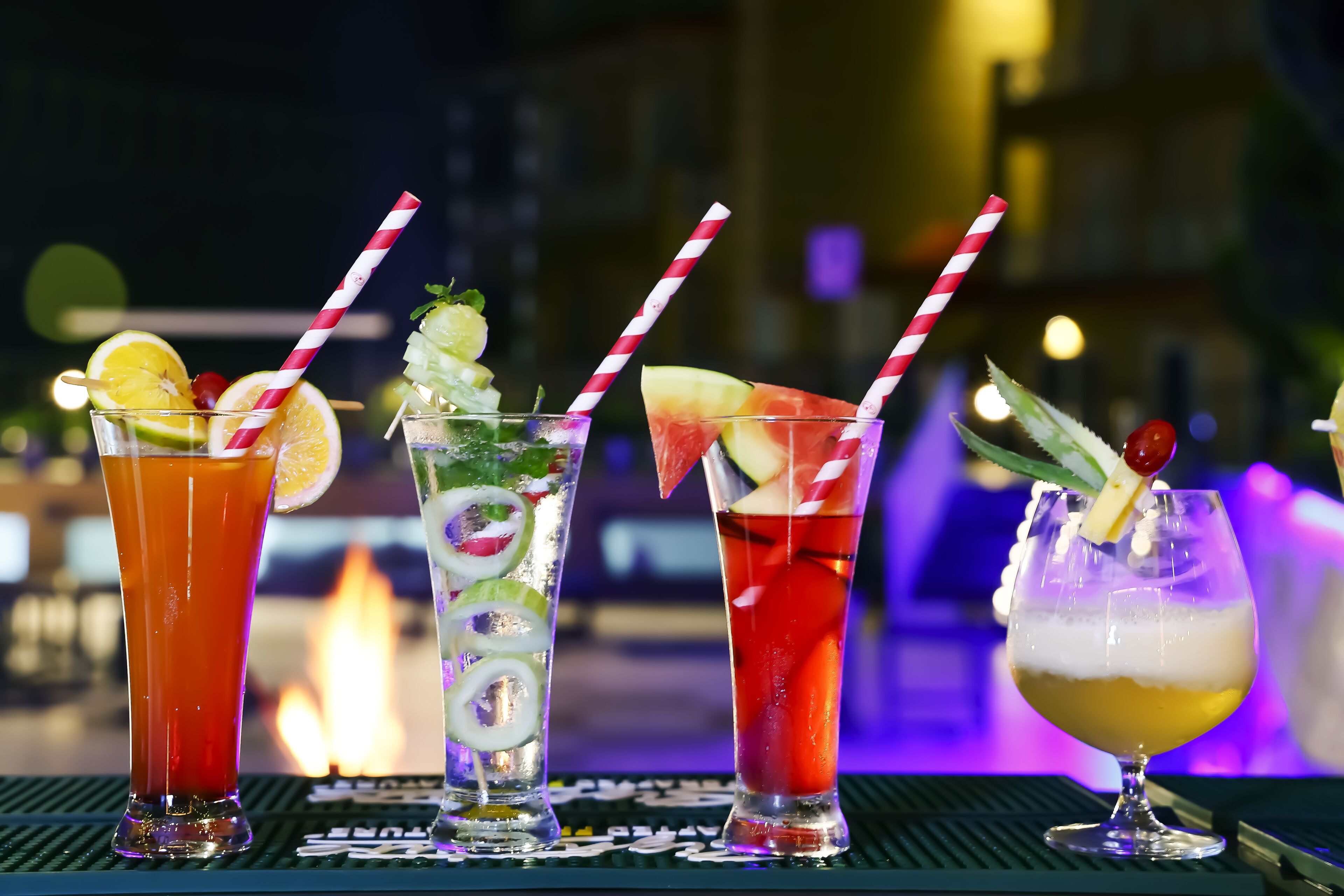 Four cocktails with straws and garnishes on a bar counter.
