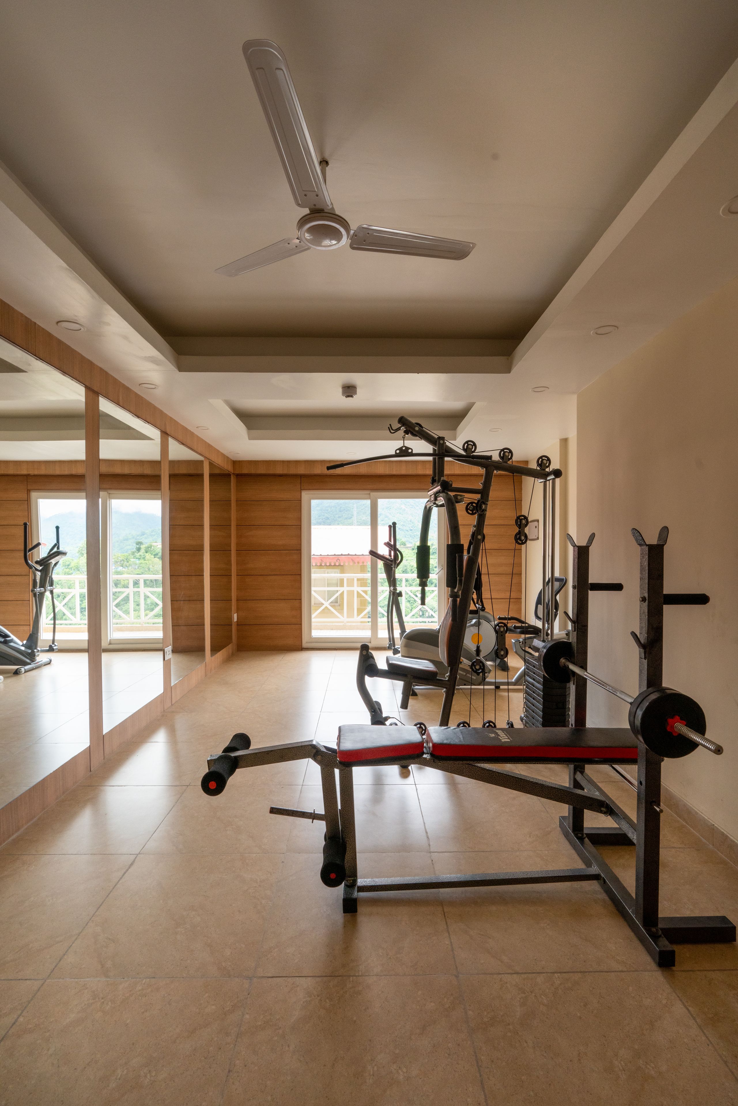 A gym with exercise equipment, large windows, and a ceiling fan.