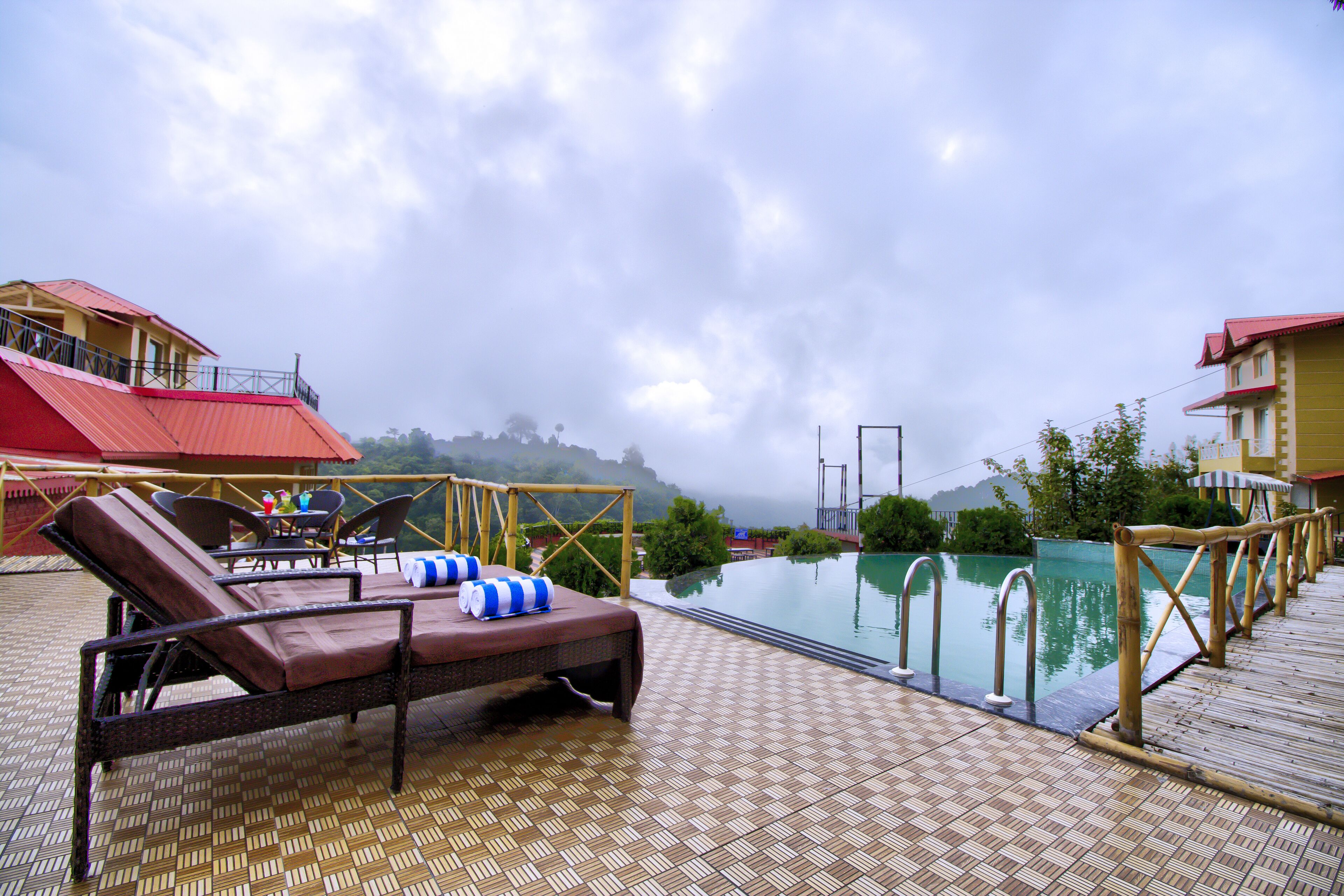 A poolside area with lounge chairs and a small table, surrounded by a wooden deck and a view of a mountain in the background.