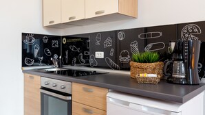 A modern kitchen with a black backsplash featuring white food illustrations, a coffee maker, and a basket with green plants. - Downtown Zagreb Apartments (Zagreb)