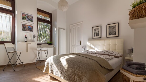 A bedroom with a large bed, a desk, and a window with blinds. - Downtown Zagreb Apartments (Zagreb)
