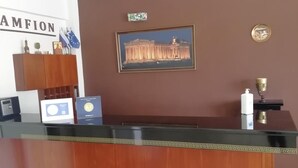 A reception desk with a framed picture of a historical building, a plaque, and a small trophy on the wall. - Amfion Hotel (Katerini)