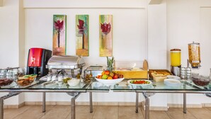 A buffet setup with various food items, a coffee machine, and decorative paintings on the wall. - Amfion Hotel (Katerini)