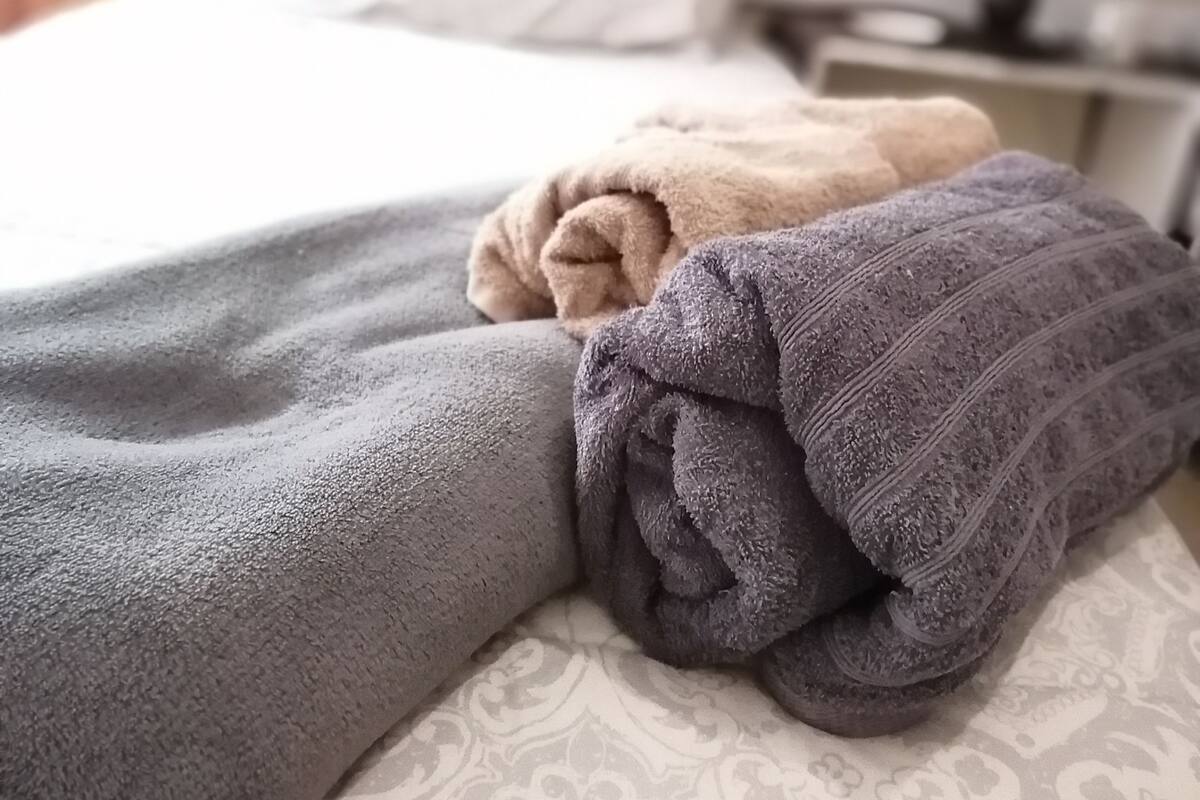 A neatly made bed with a grey blanket and two folded blankets in different shades.