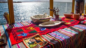 A table with colorful textiles and traditional pottery, set against a view of a calm sea.
