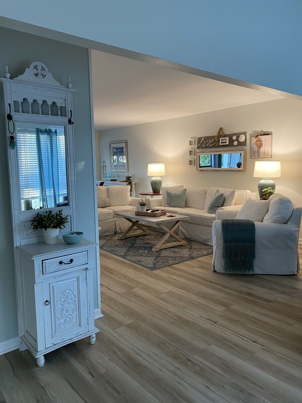 A living room with a white sofa, a coffee table, a white cabinet, and a mirror. - Beautiful One-Story Cottage Just Minutes From White Sand Beach, with Golf Cart! (Destin)