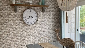 A rustic dining area with a brick wall, a large wall clock, wooden furniture, and a hanging light fixture. - Beautiful One-Story Cottage Just Minutes From White Sand Beach, with Golf Cart!  (Destin)