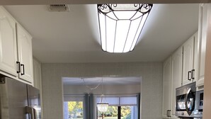 A modern kitchen with white cabinets, stainless steel appliances, and a window with a view of a green landscape. - Beautiful One-Story Cottage Just Minutes From White Sand Beach, with Golf Cart!  (Destin)