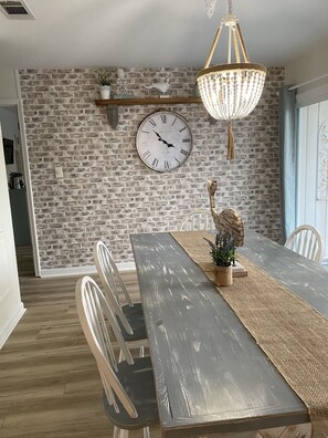 A dining area with a rustic brick wall, a large wall clock, and a chandelier. - Beautiful One-Story Cottage Just Minutes From White Sand Beach, with Golf Cart! (Destin)
