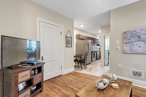 A modern living room with a flat-screen TV, wooden entertainment unit, and a dining area with a wooden table and chairs. - Luxury Condo down the street from Tower Grove Park (St. Louis)