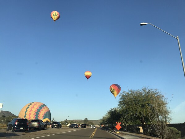 Une rue bordée de voitures garées et survolée par des montgolfières.
