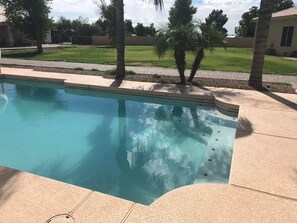 Una piscina de borde curvo, rodeada por un solárium empedrado.