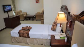 Una habitación de hotel con cama, escritorio con lámpara, televisor y sofá.