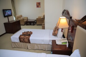 A hotel room with a bed, a desk with a lamp, a television, and a sofa.