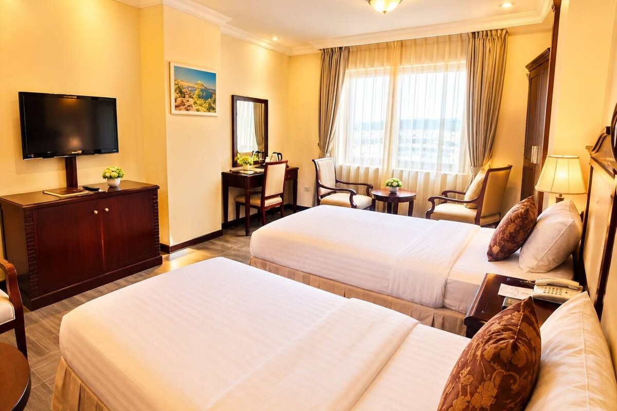 A hotel room with two beds, a desk, a television, and a window with curtains.