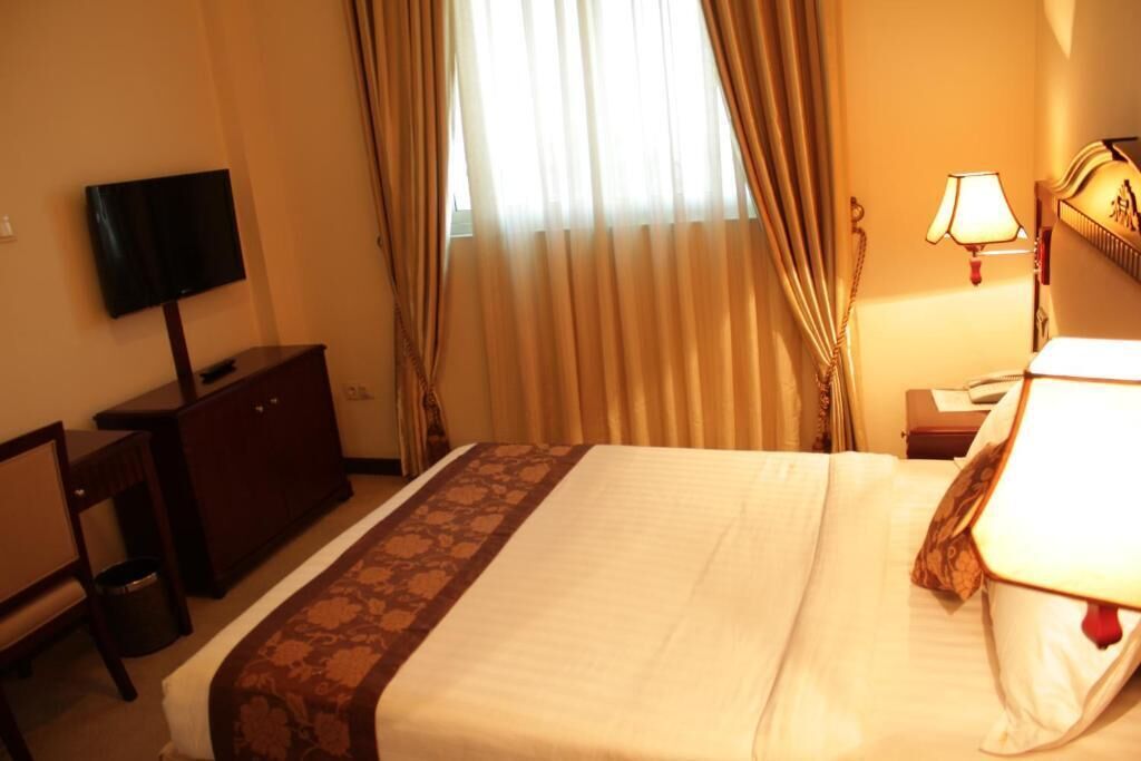 A hotel room with a bed, a television, a desk, a lamp, and curtains.