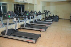A row of treadmills in a gym with a mirrored wall and a tiled floor.