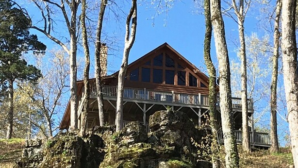 A wooden cabin with a balcony, surrounded by trees and rocks.