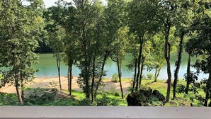 A view of a lake surrounded by trees, with a sandy beach and a wooden deck in the foreground.