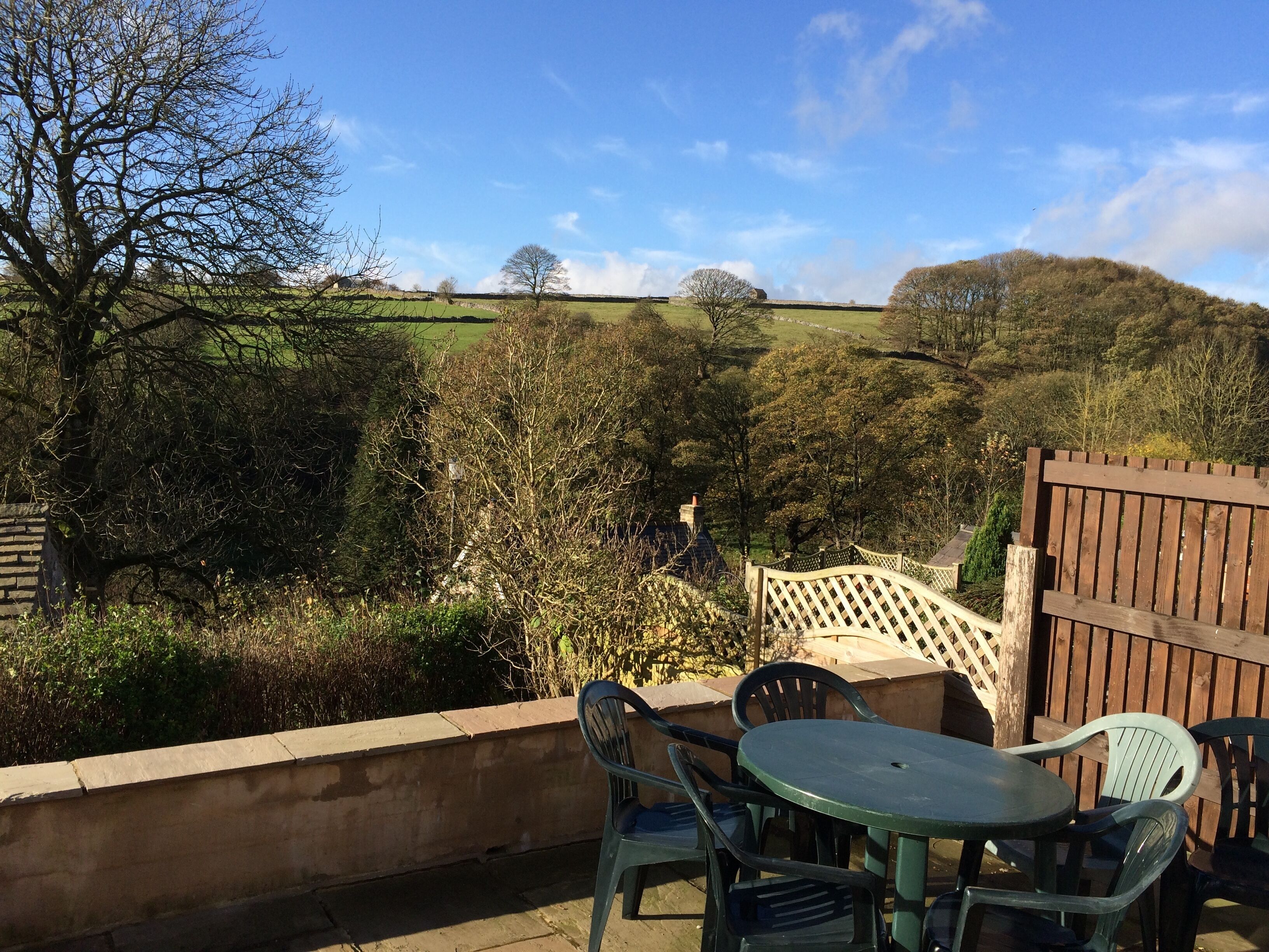 A patio with a round table and chairs, overlooking a rural landscape with trees and hills.