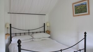 Een net opgemaakt bed met witte lakens en twee bedlampjes, een ingelijste foto aan de muur en een witte gordijn boven het bed.